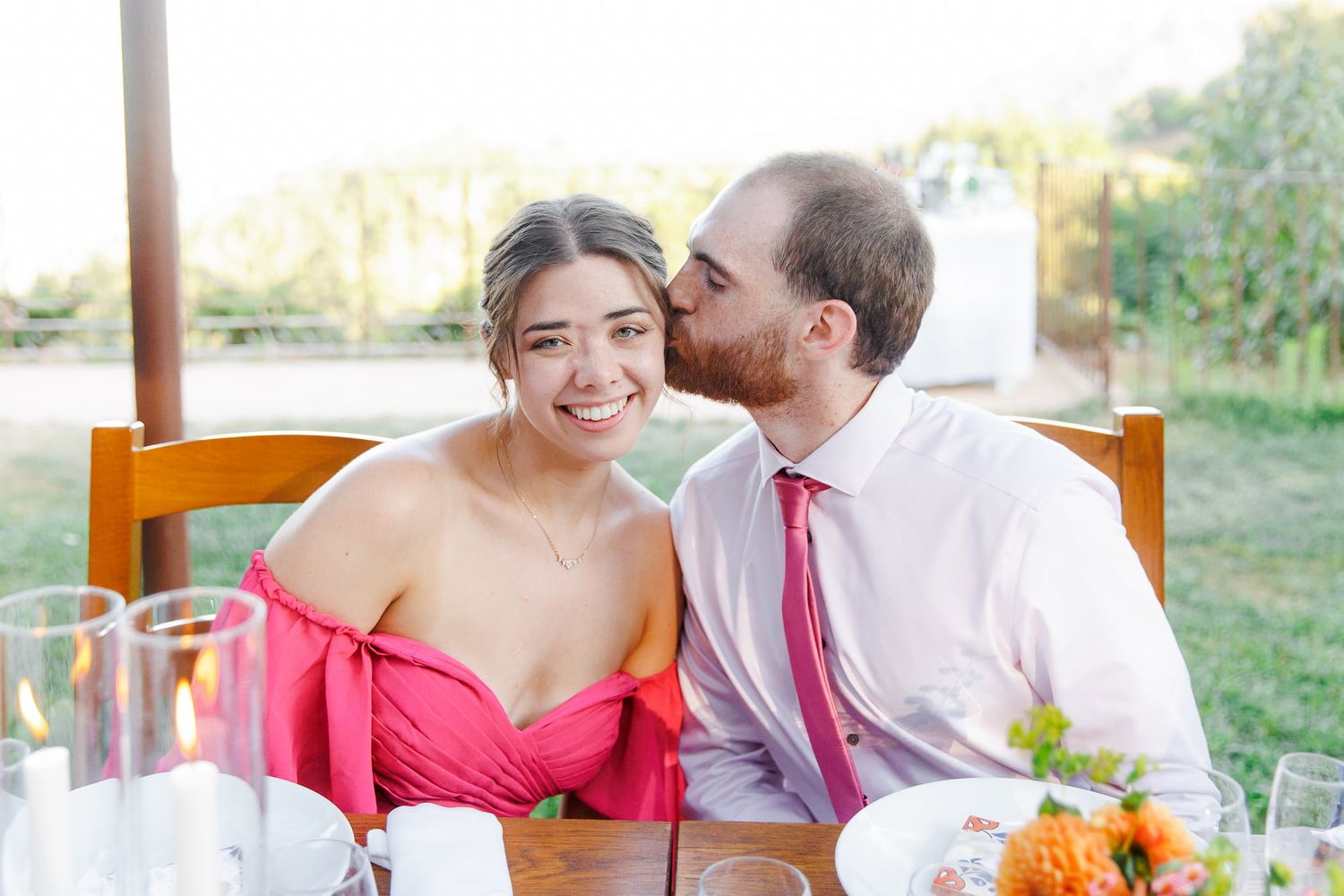 A romantic couple in pink and white attire sharing intimate moments during an outdoor wedding celebration.