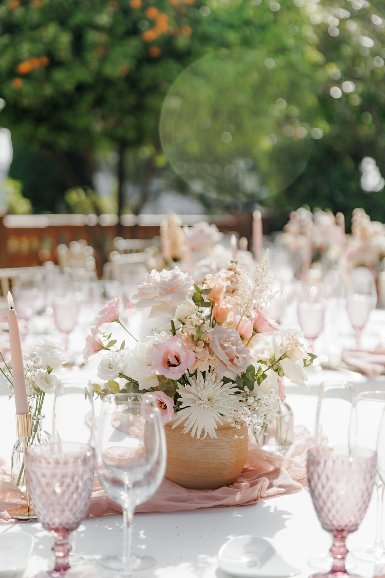 Decorated wedding table centerpiece with pink and white flowers, blush napkins, and pink glassware outdoors.