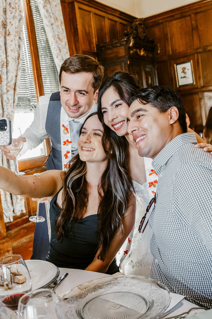 Four friends taking a selfie together at an elegant dining table during a formal celebration event.