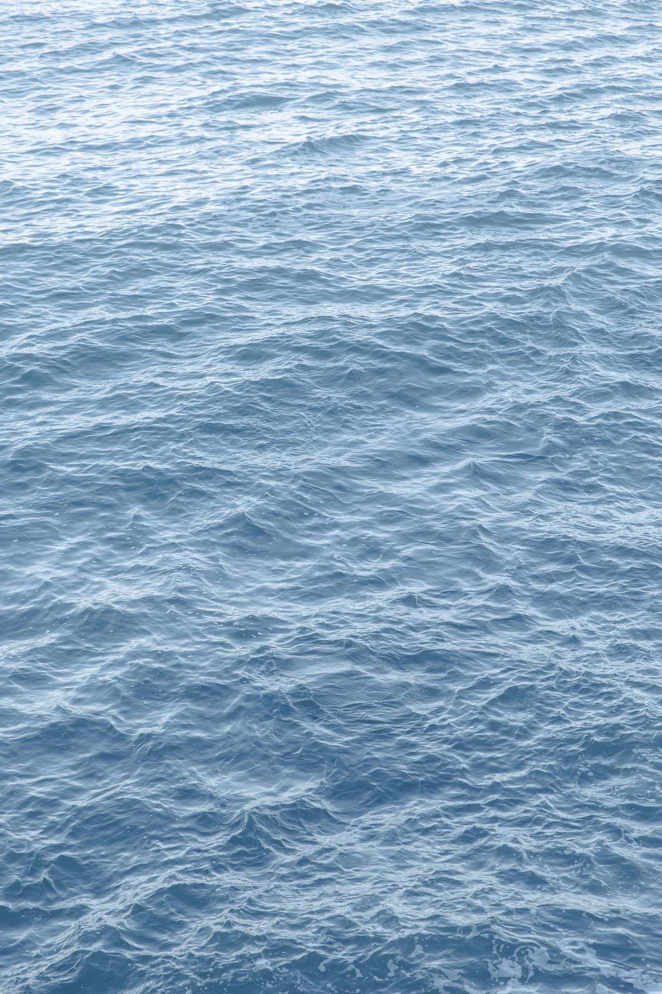 Calm blue ocean water surface with gentle ripples and waves creating a serene nautical background texture.