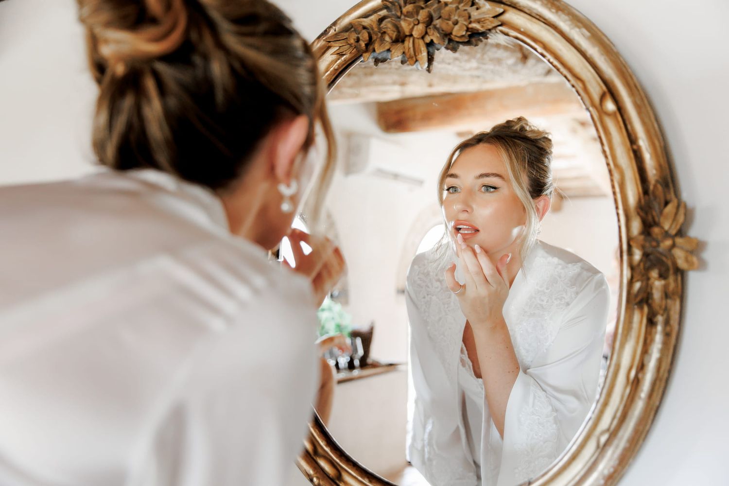 Young bride in a white robe applying lip gloss. wedding photo idea