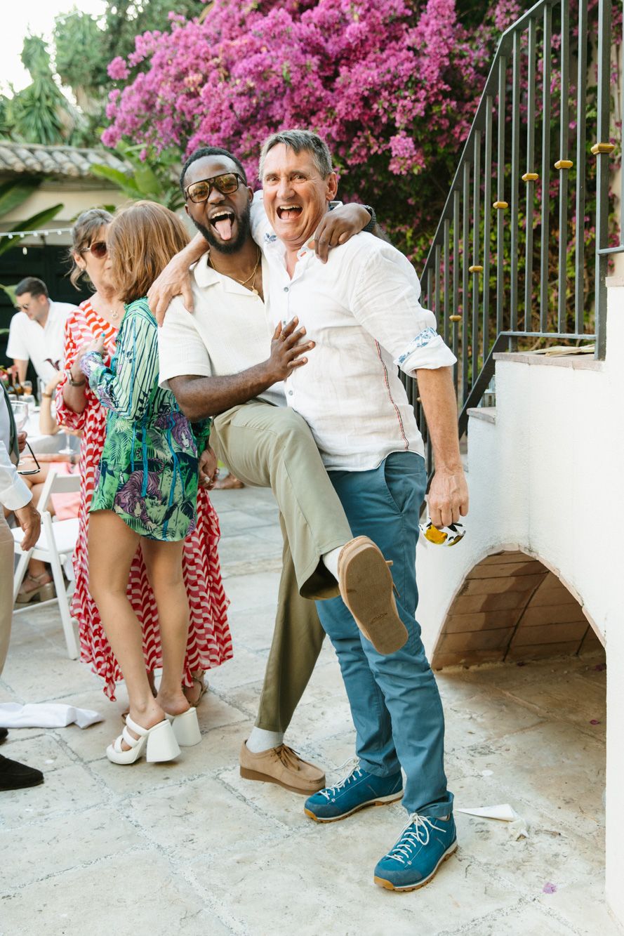 Three friends laugh and pose together at an outdoor party with pink bougainvillea flowers in the background.