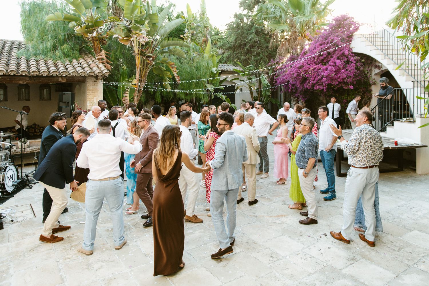 Guests dancing outdoors at a wedding reception in a Mediterranean courtyard with bougainvillea and string lights.