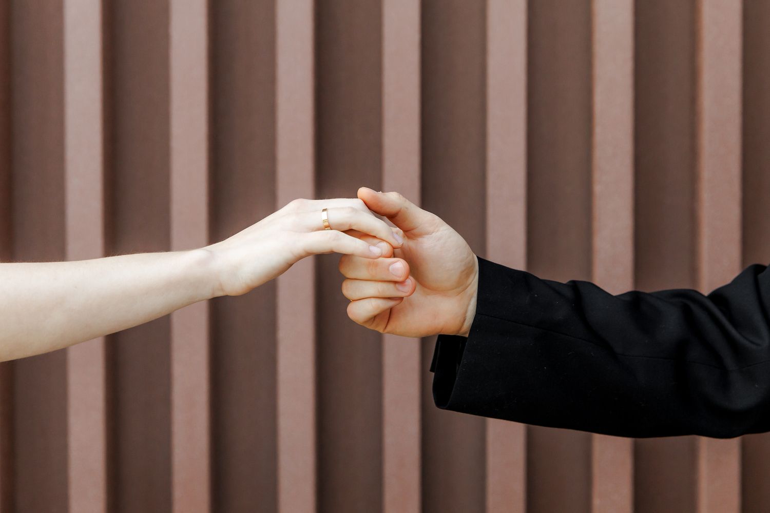 Two people gently holding hands against a striped brown wall, symbolizing connection and togetherness.