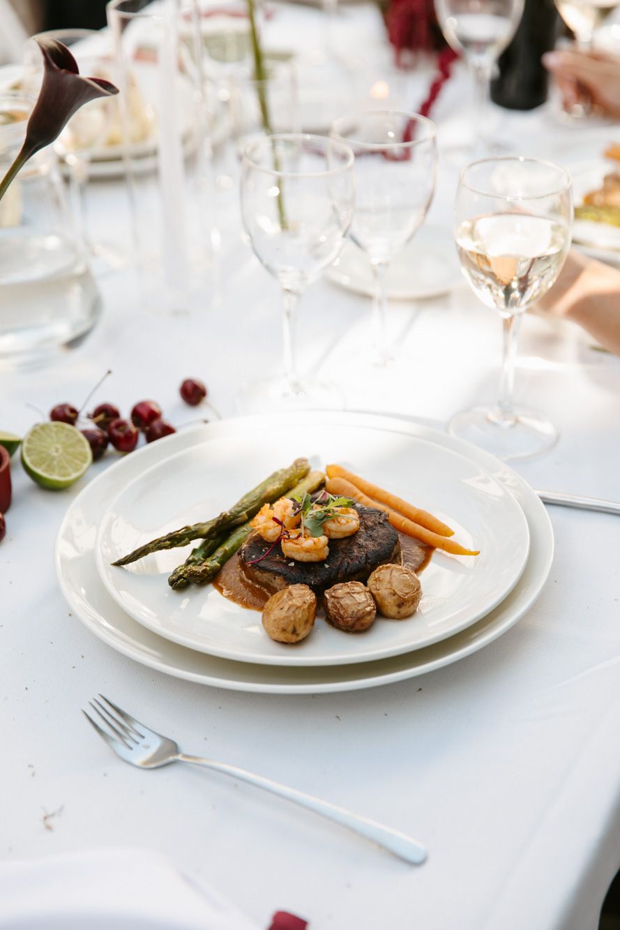 Elegant plated steak with asparagus, carrots, shrimp, and roasted potatoes on white china at a formal dinner.