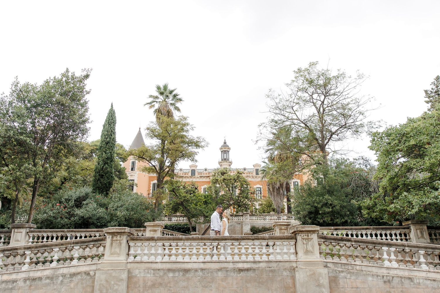 Landscape photo of the engaged couple looking at each other in front of Palau le les Heures.