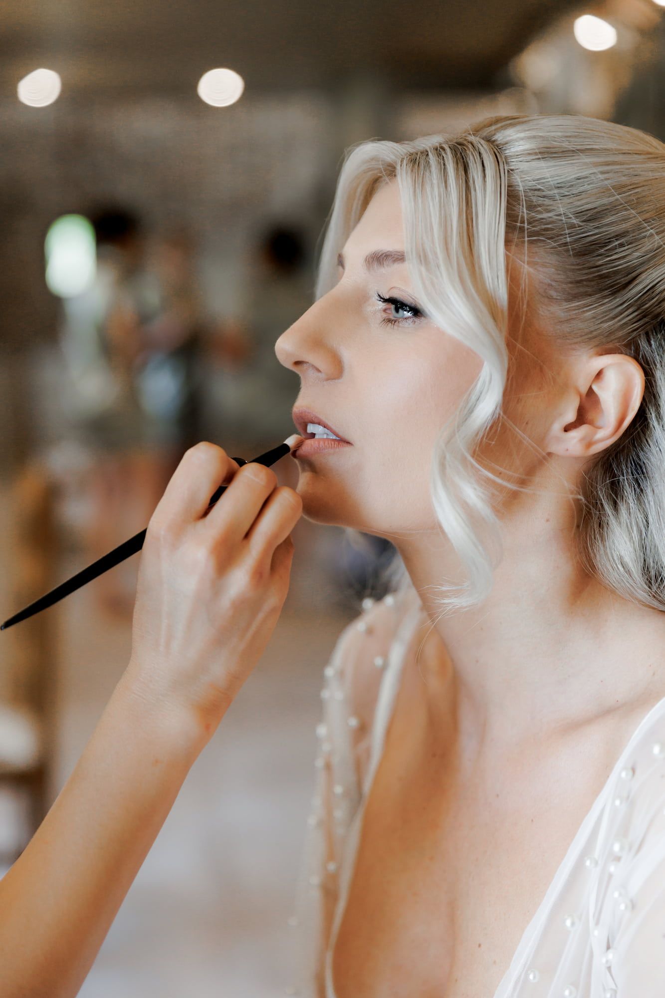 A makeup artist applying lipstick to a bride with a lip brush during bridal preparations at wedding venue in Barcelona