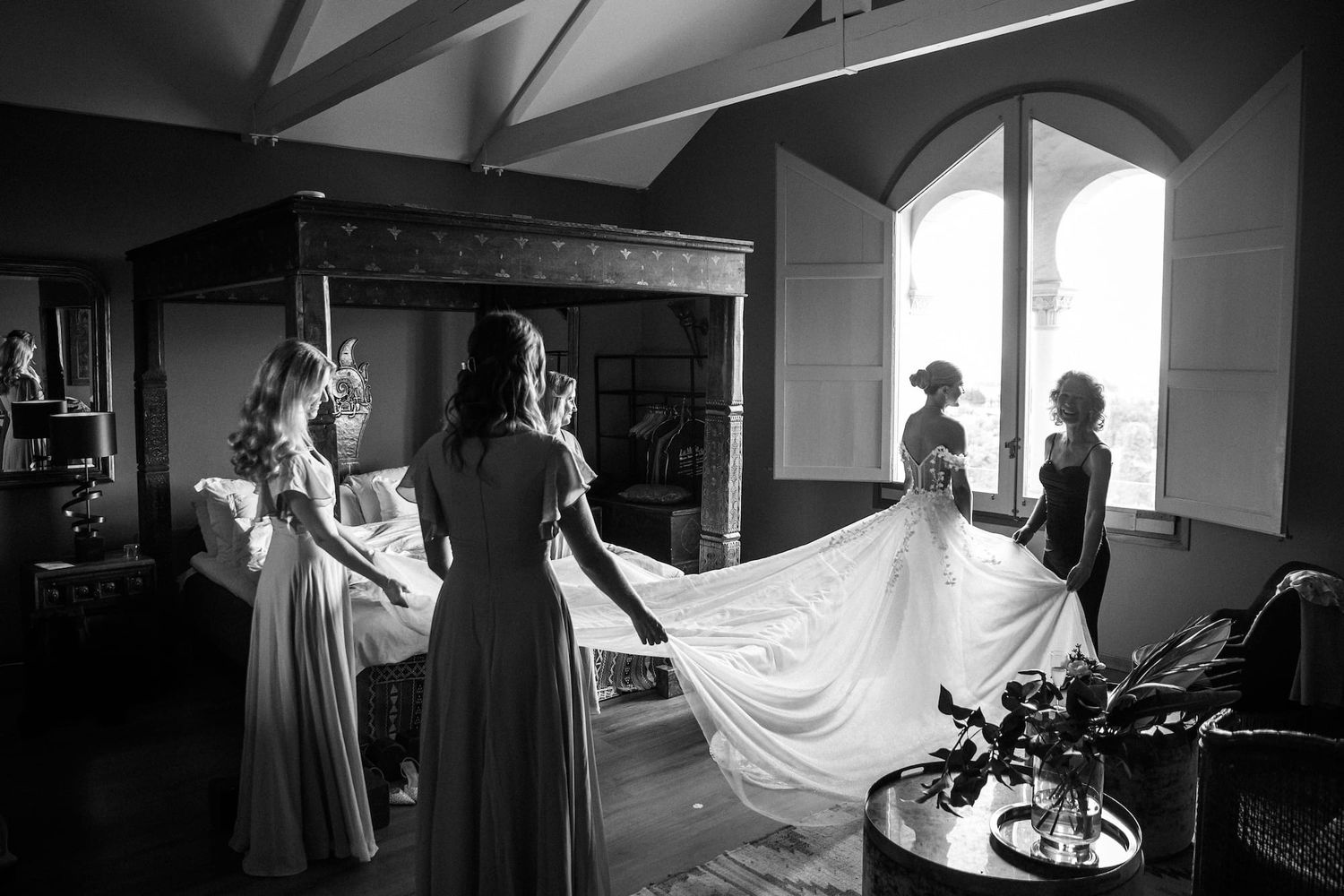 Black and white photo of bridesmaids helping bride with wedding gown train in elegant room of the wedding venue in Barcelona