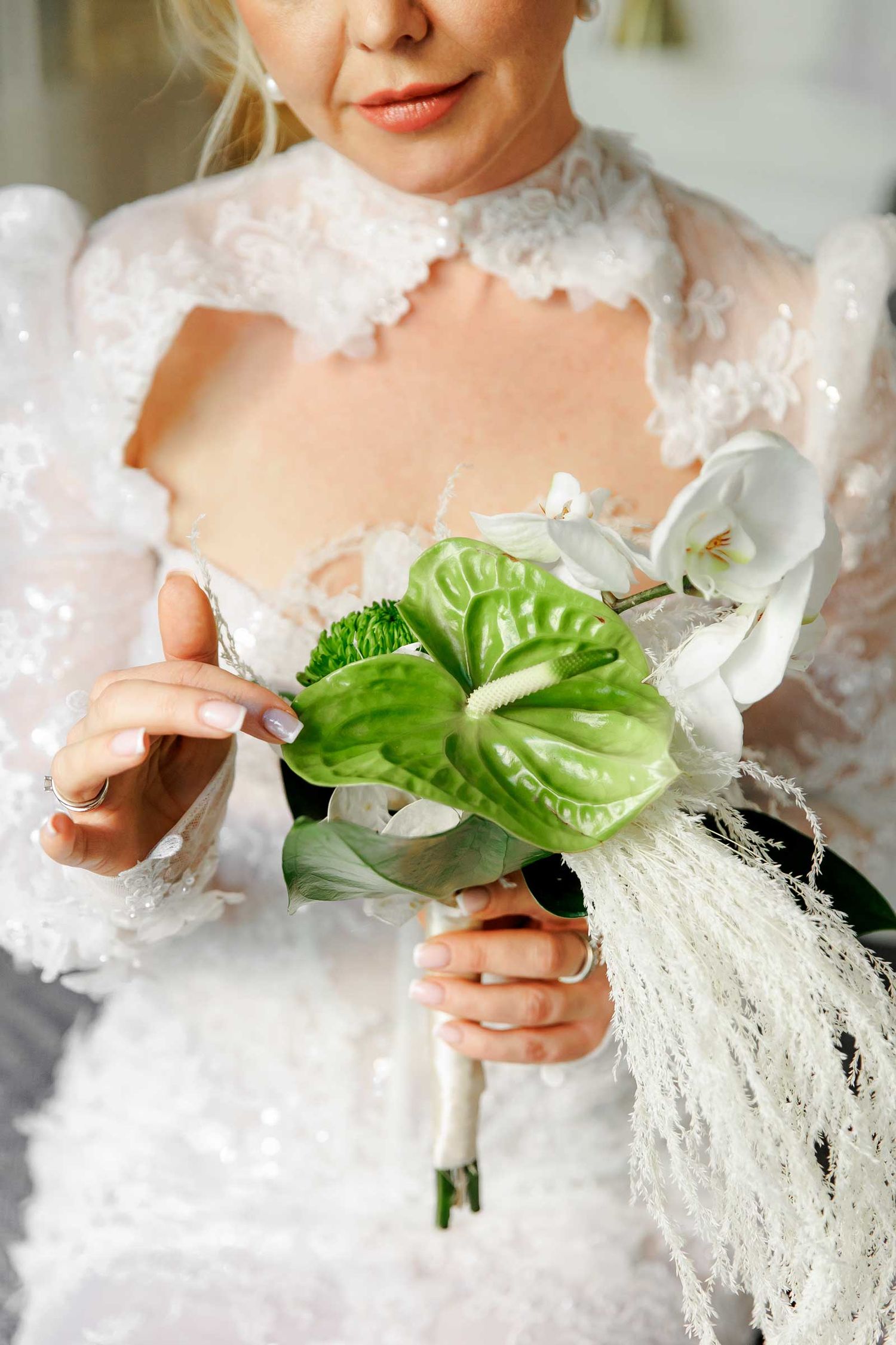 The bride holds her bouquet and looks at the green calla lilies closely.