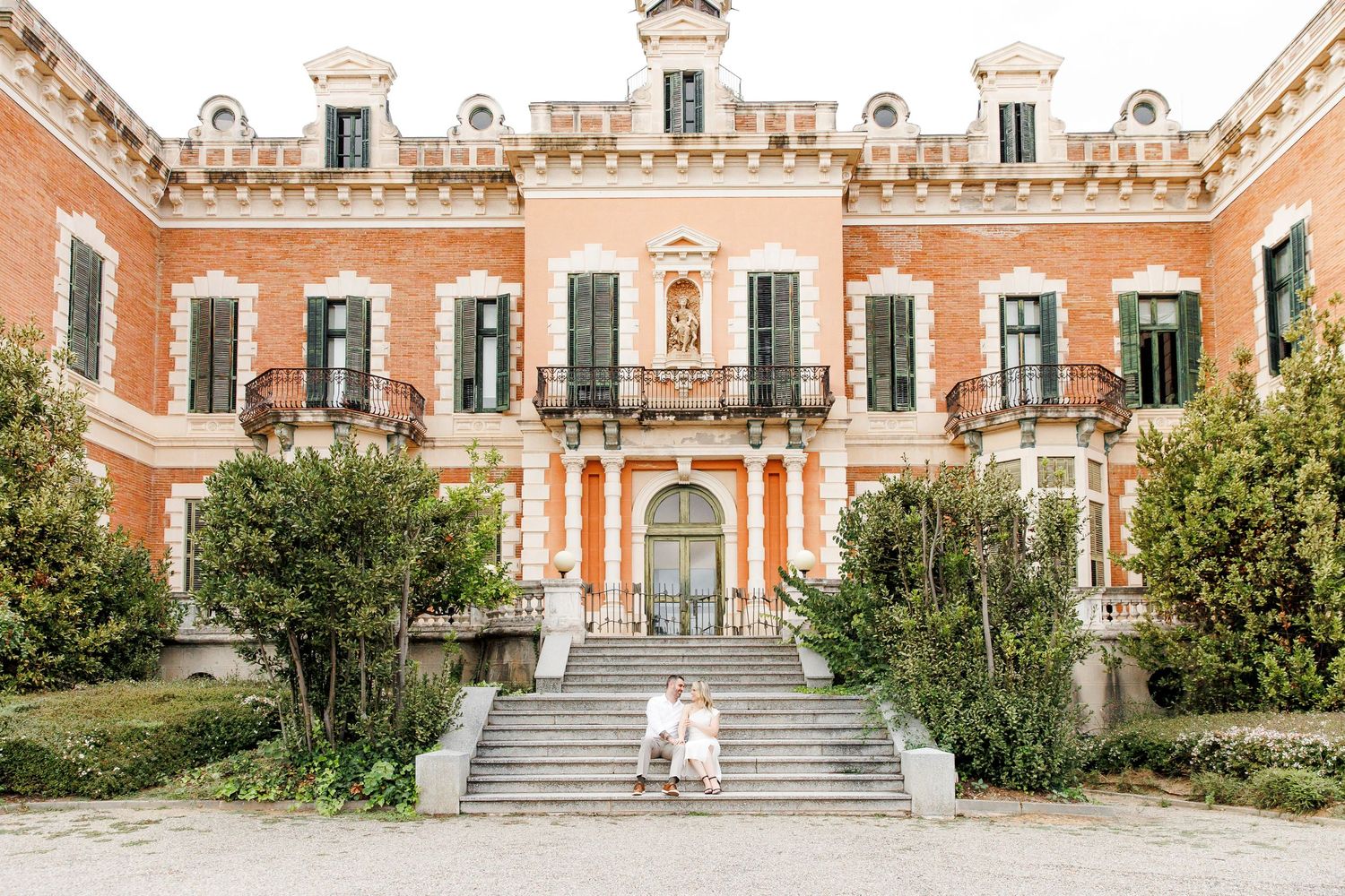 The bride and groom are seated on the stairs at the main entrance of the castle.