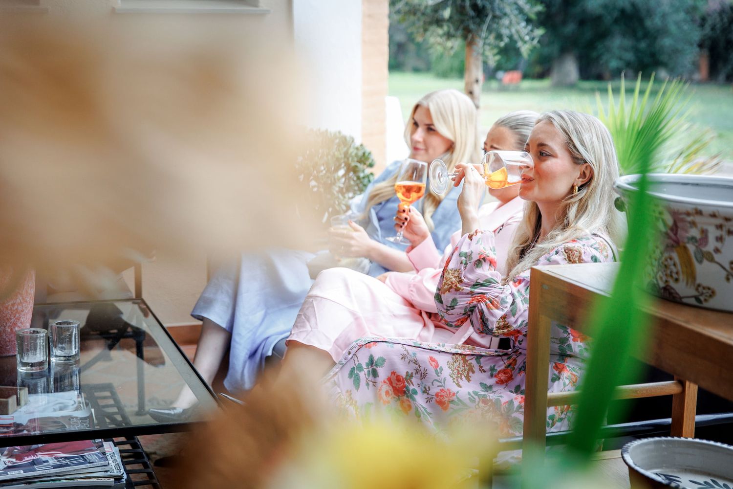 Two women in floral robes sipping cocktails together in a bright, elegant lounge setting.