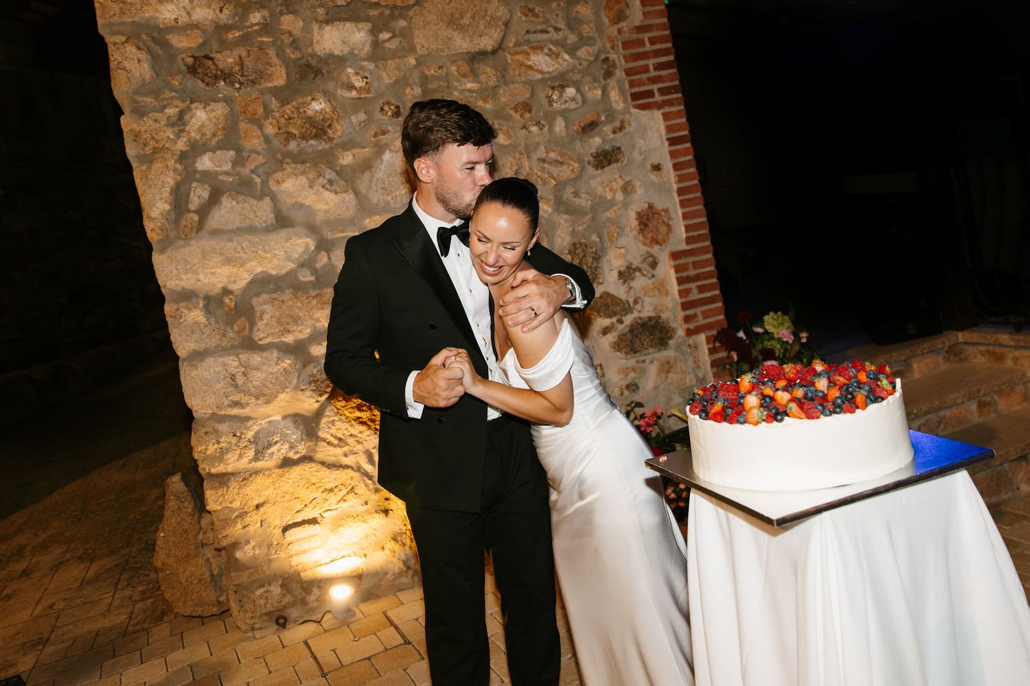 Bride and groom share a joyful moment cutting their wedding cake at an elegant outdoor evening reception.