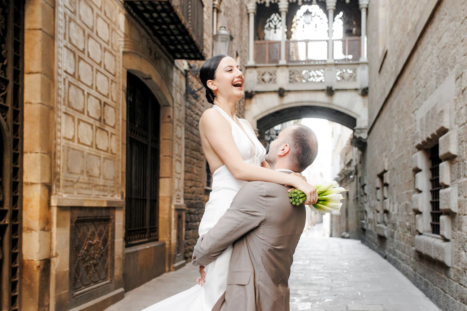 A couple shares a joyful moment in the Gothic Quarter as the groom lifts the bride in her white dress.