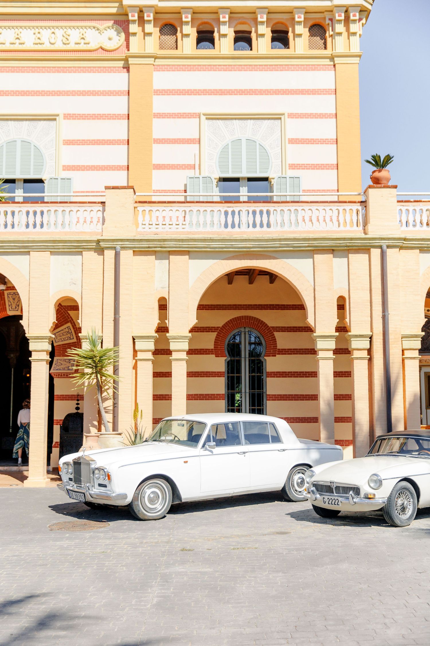 Two white vintage cars are parked in front of the villa.