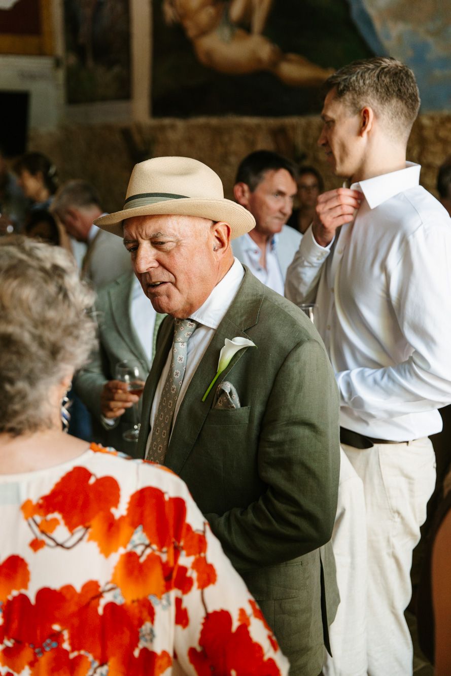 Elderly man in green suit and panama hat socializing at an elegant outdoor wedding reception.