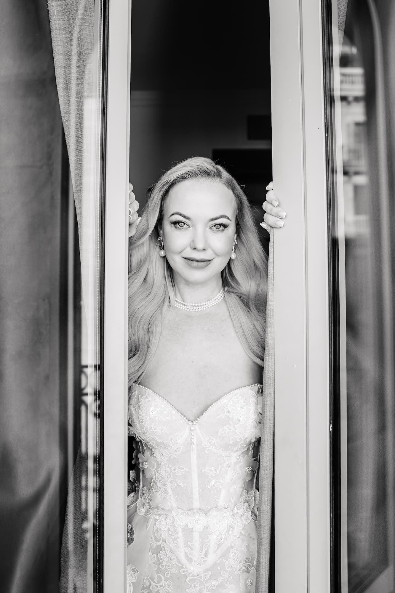 A bride in a white wedding dress poses through a window pane, creating an artistic portrait effect.