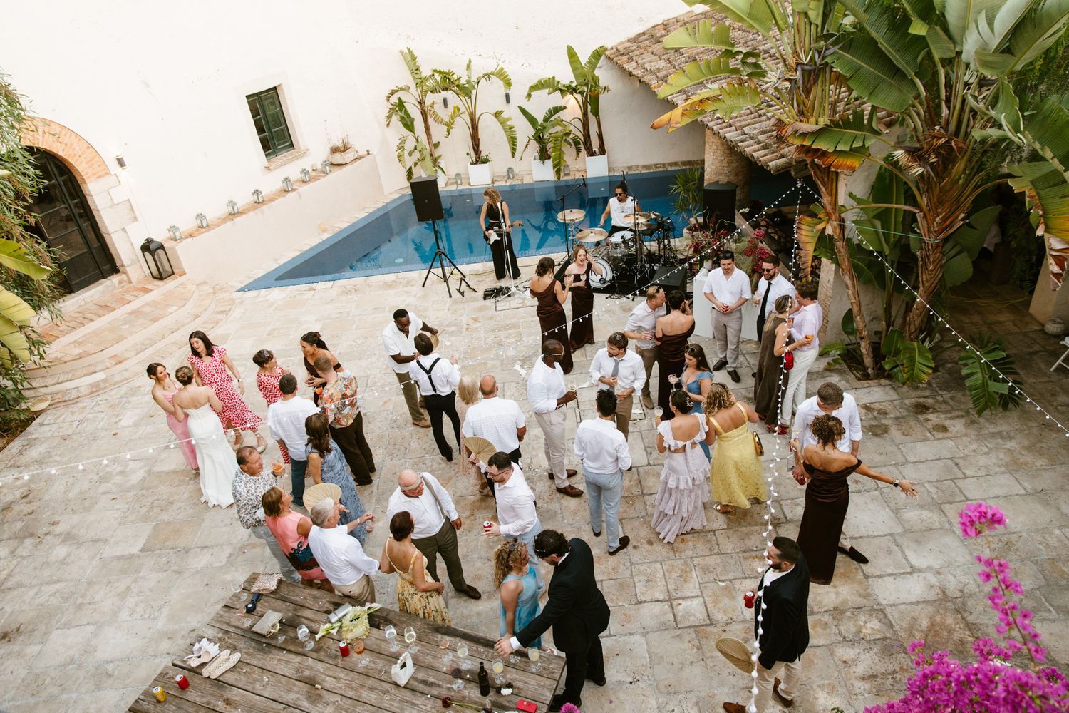 Aerial view of a wedding reception at Masia Victoria by a pool, with guests dancing on a stone patio surrounded by tropical plants.