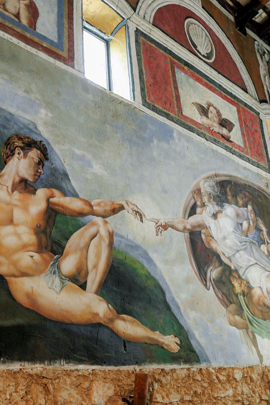 Michelangelo's Creation of Adam fresco reproduction on a wall, depicting God reaching toward Adam.