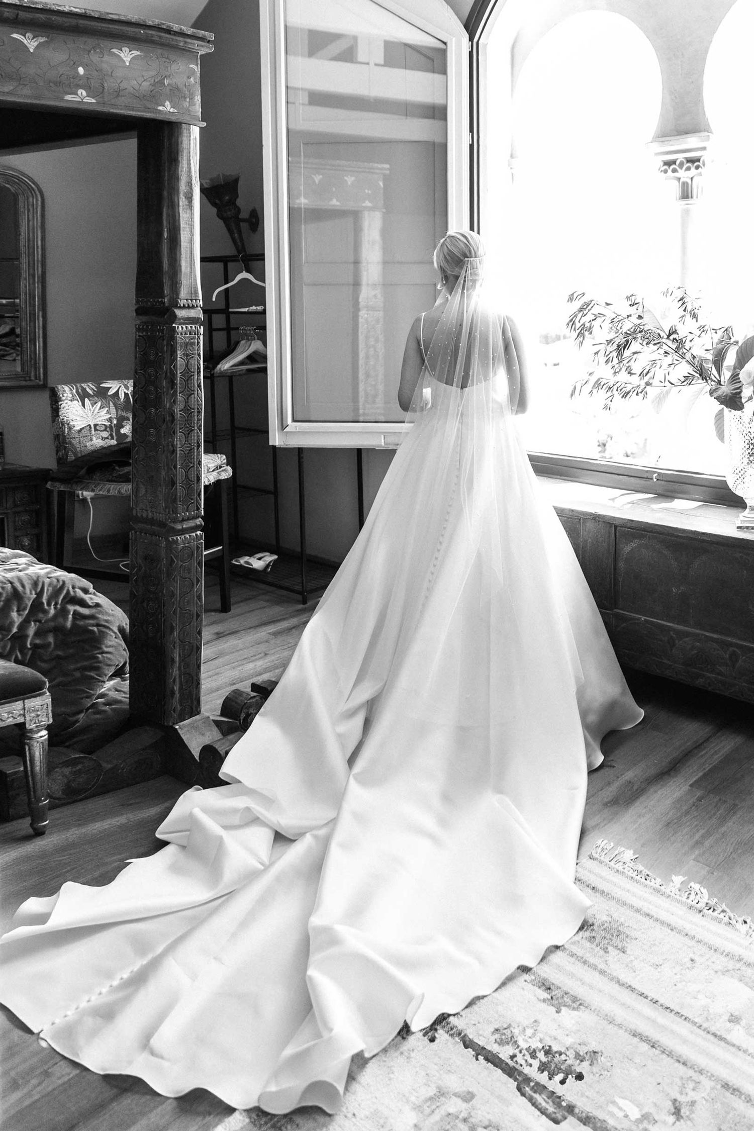 A bride in the long white wedding dress looking in the window and waiting for the moment for the ceremony to start