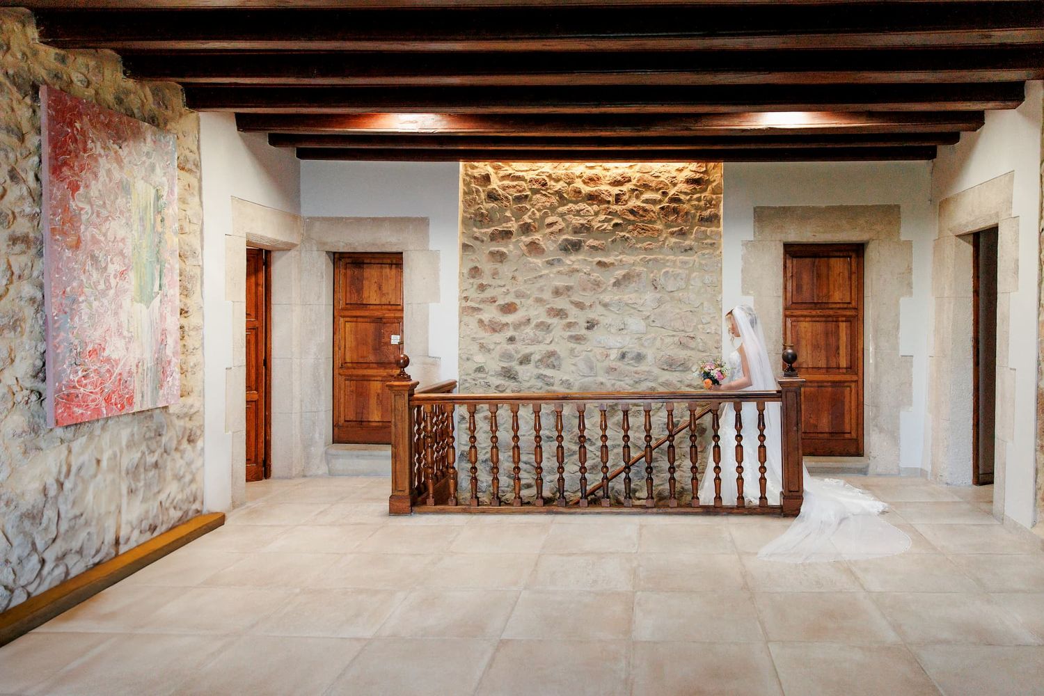 Rustic hallway with exposed wooden beams, stone walls, and wooden doors leading to multiple interior spaces.