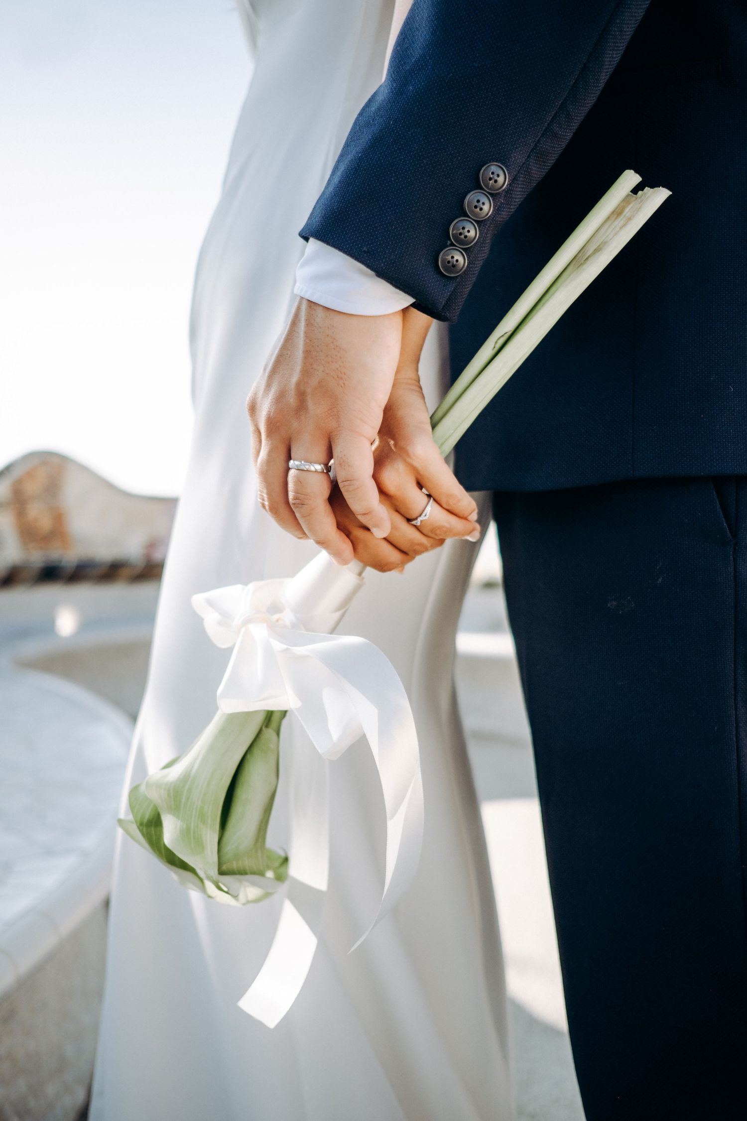 The groom holds the bride’s hand, highlighting her ring and the bridal bouquet.