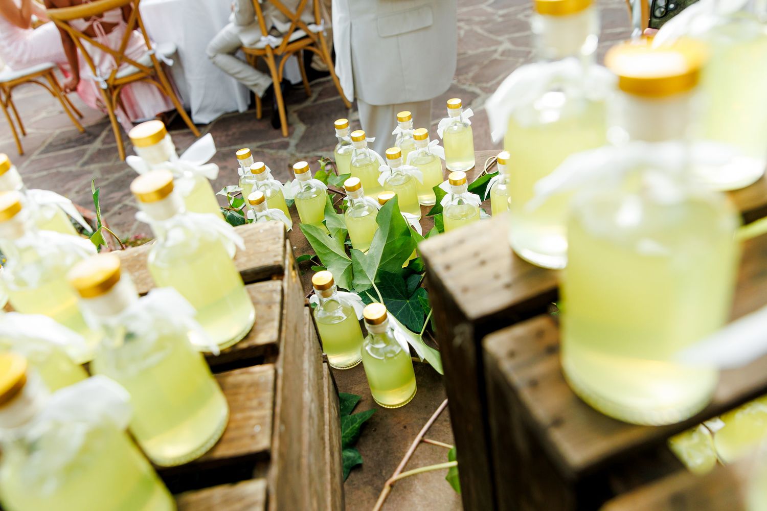 Rows of small bottles filled with limonchello, decorated with green leaves at a wedding.
