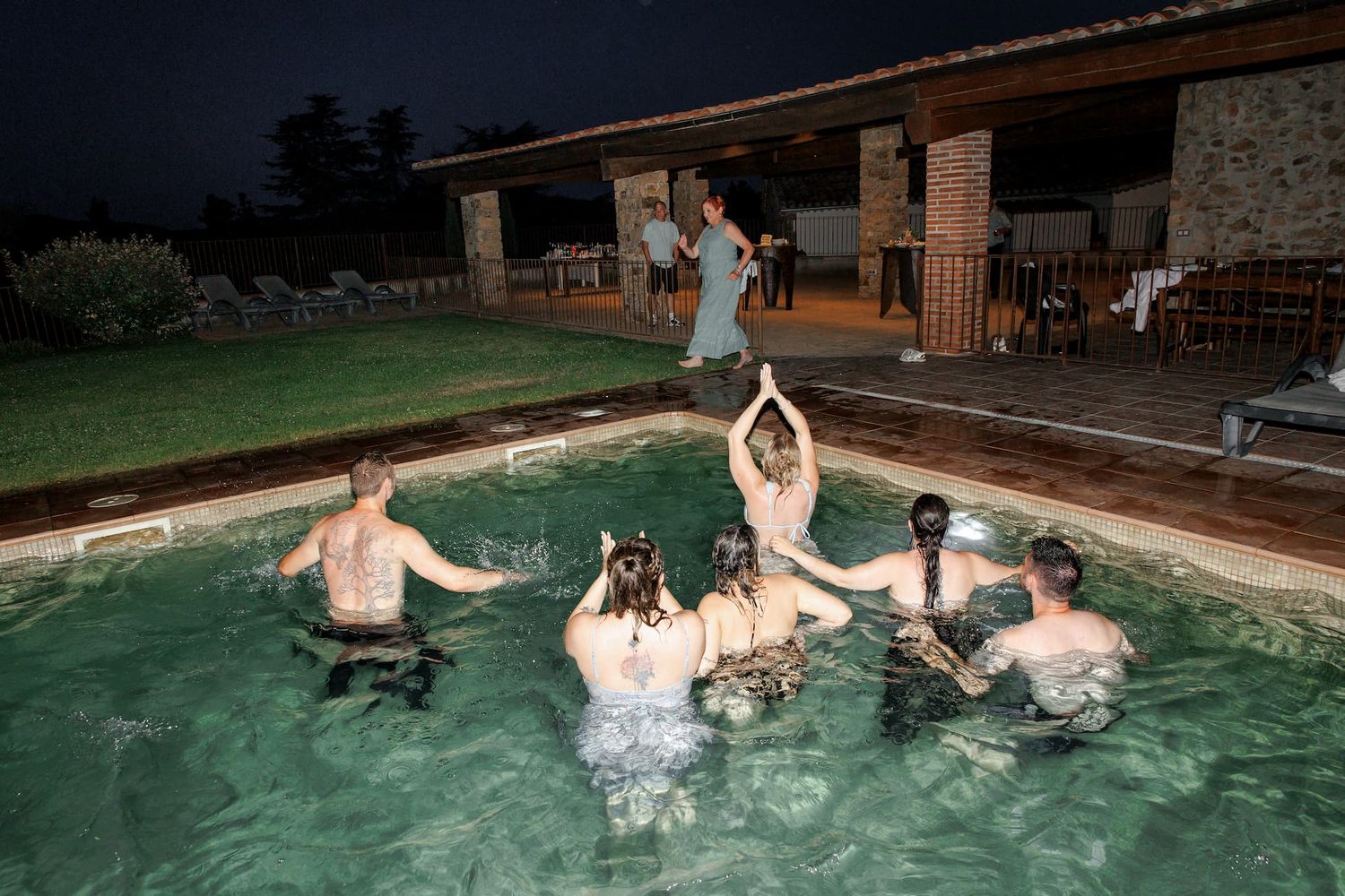 Wedding guests enjoying a fun moment in a swimming pool at night.