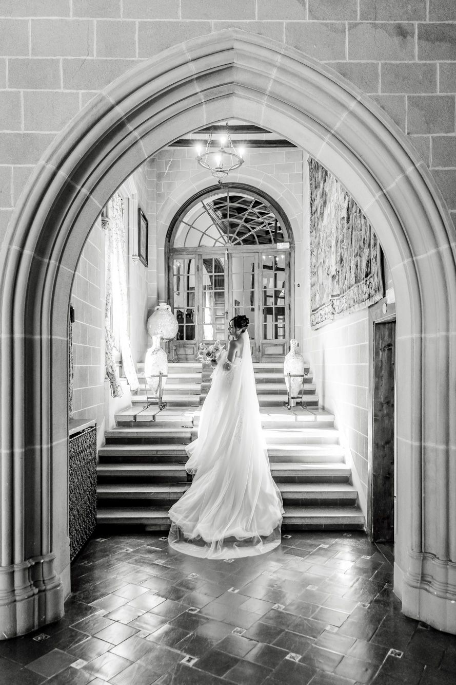 Black and white photo of a bride in a flowing gown standing under an arch in La Baronia wedding venue.