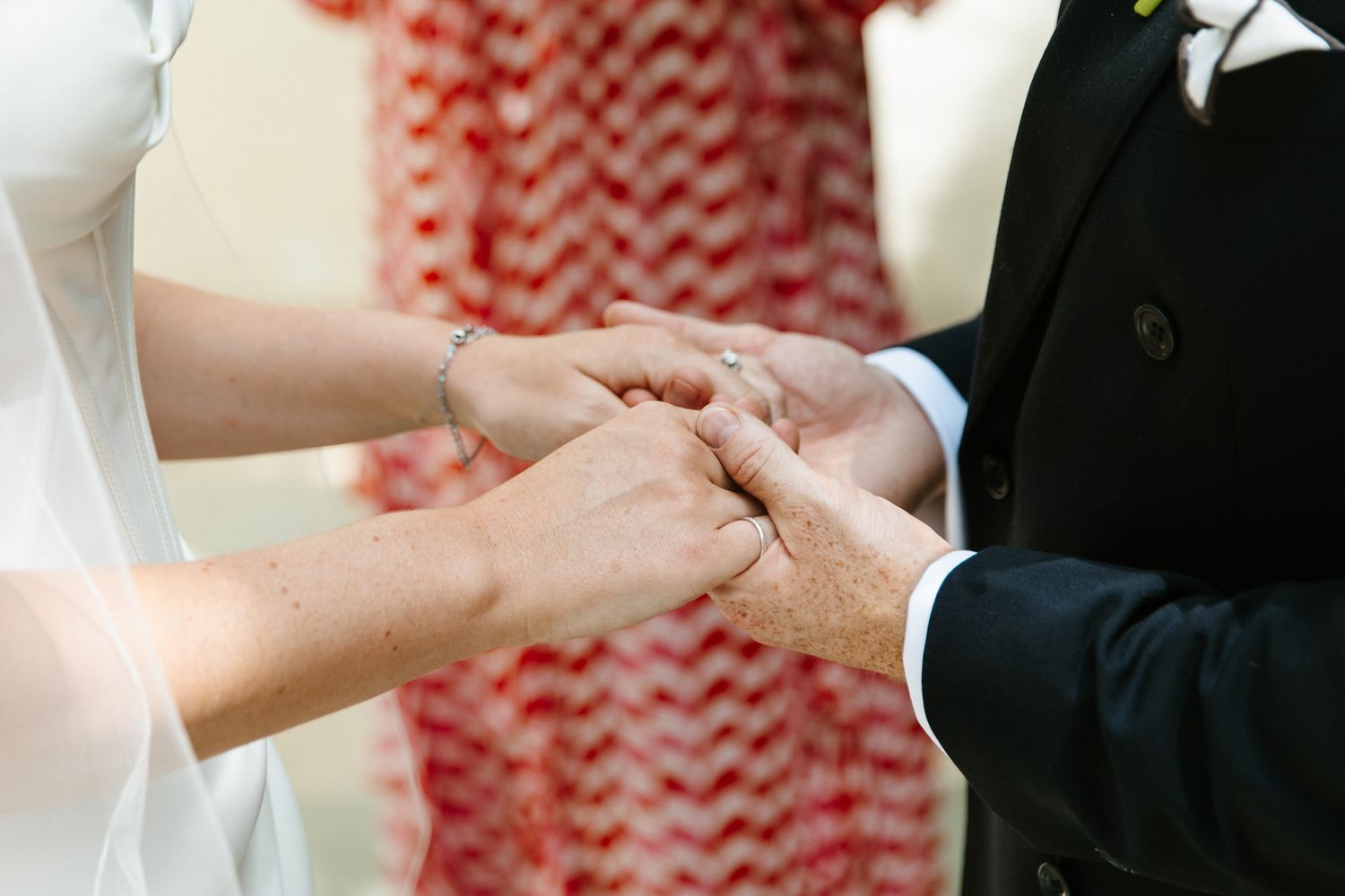 Close-up of bride and groom exchanging rings during outdoor wedding ceremony.