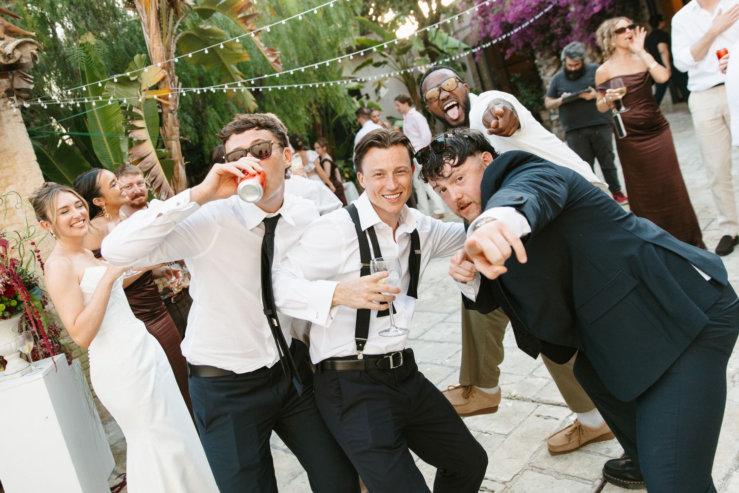 Wedding guests celebrate outdoors, posing playfully with drinks at a festive garden reception at Masia Victoria near Barcelona