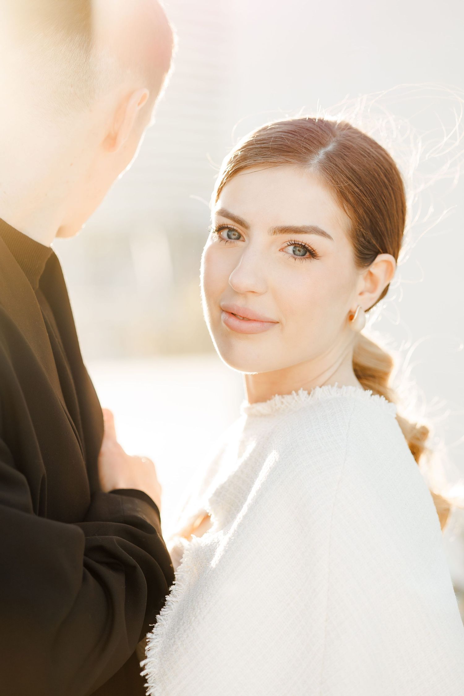A bride in a white dress gazes lovingly at her groom in a black suit during a golden hour wedding photo.