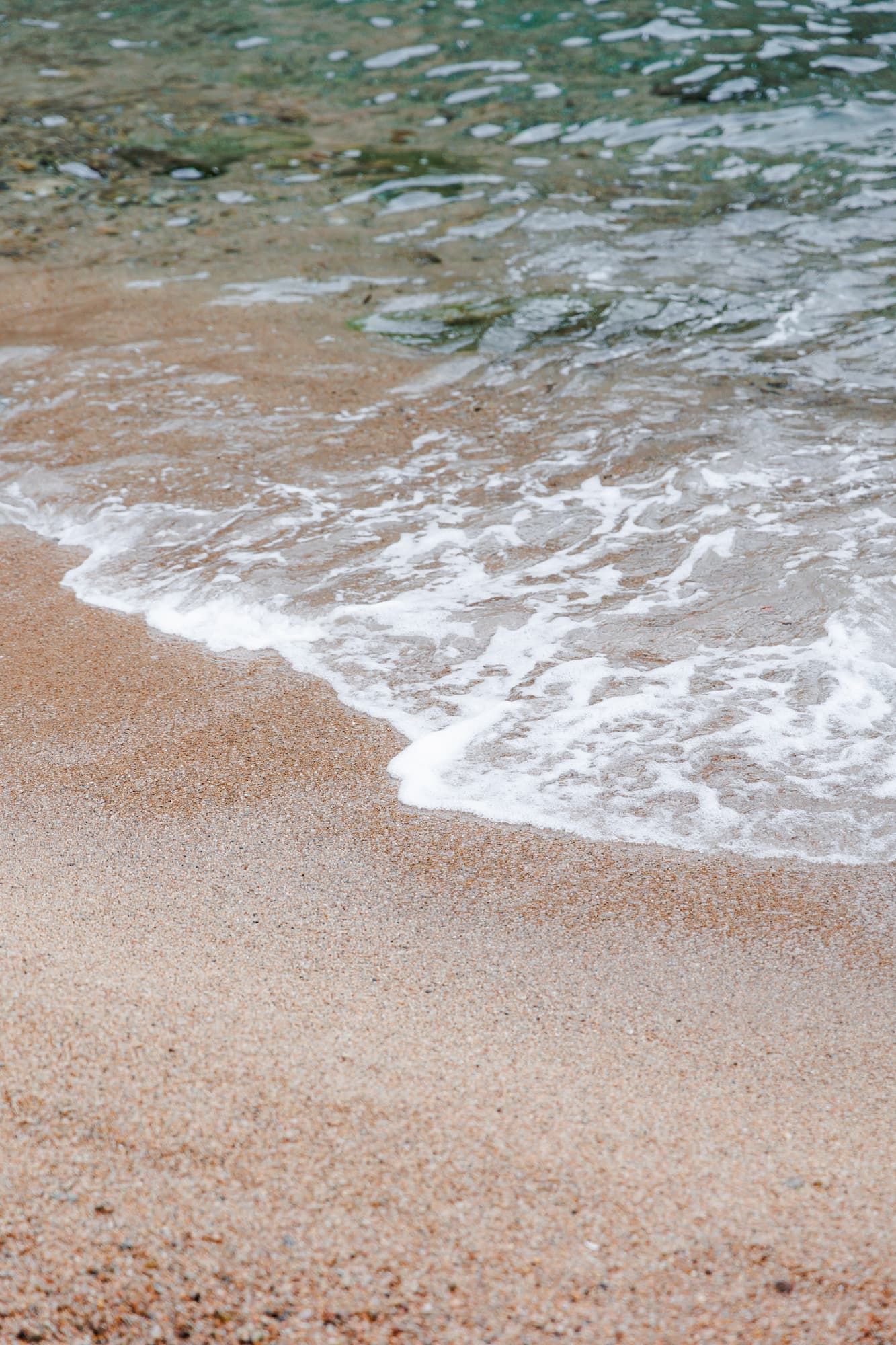 Gentle ocean waves washing up on a sandy beach shore with white foam spreading across tan colored sand.