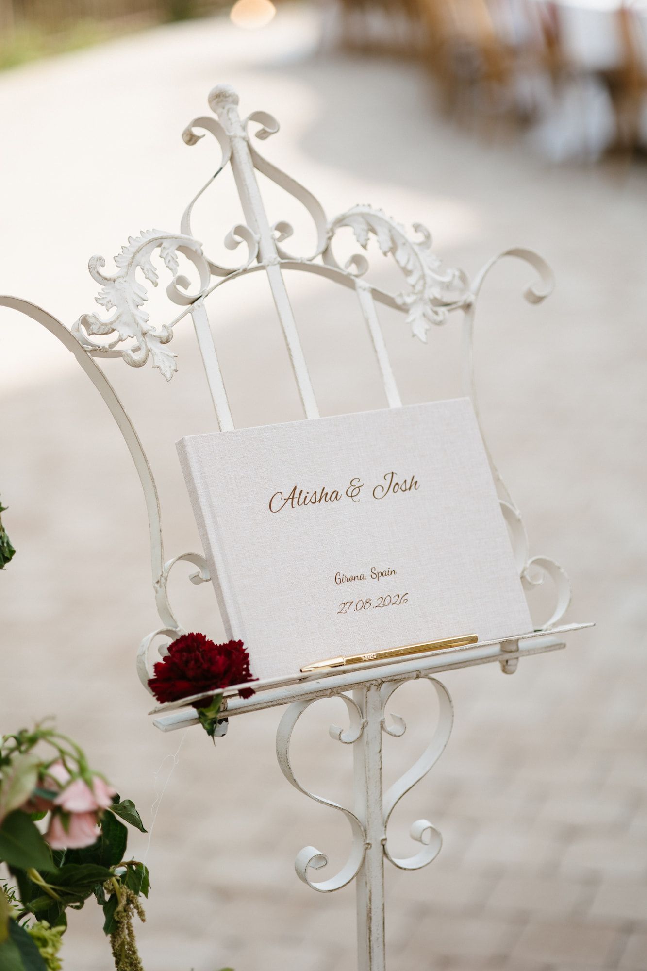 Elegant white ornate metal book stand displaying wedding program for Alisha and Josh at outdoor ceremony.
