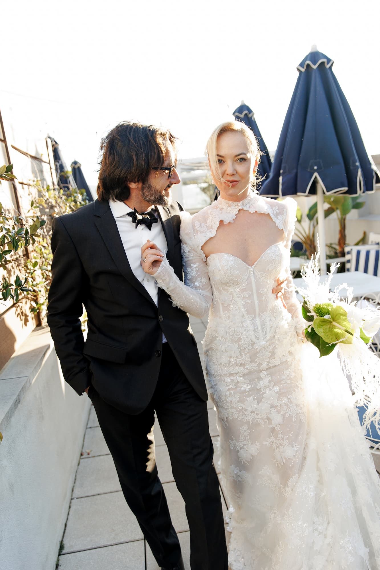 A couple in formal wedding attire pose together on an outdoor terrace in Barcelona.