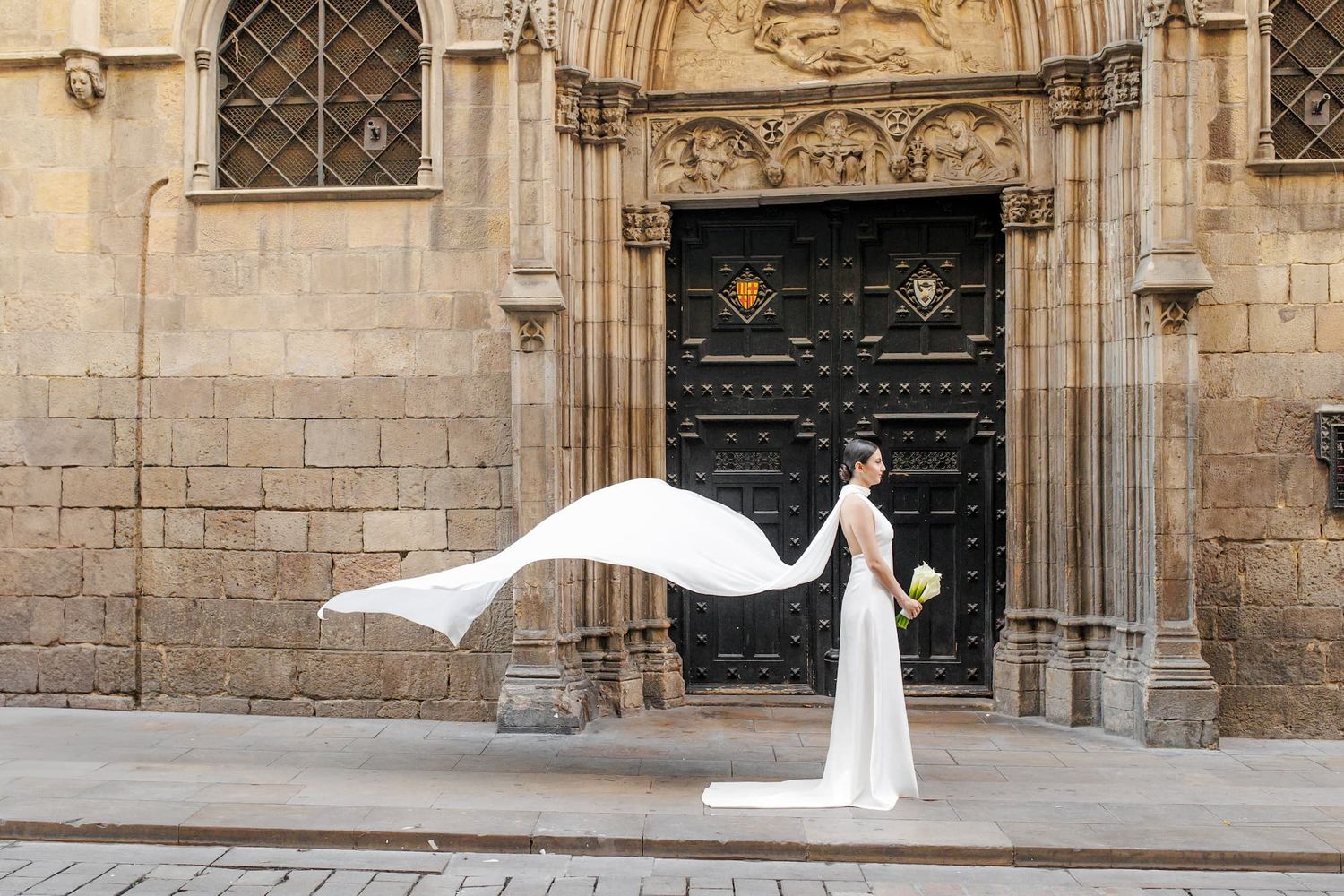 A bride in a flowing white wedding dress poses gracefully in front of an ornate stone church entrance.