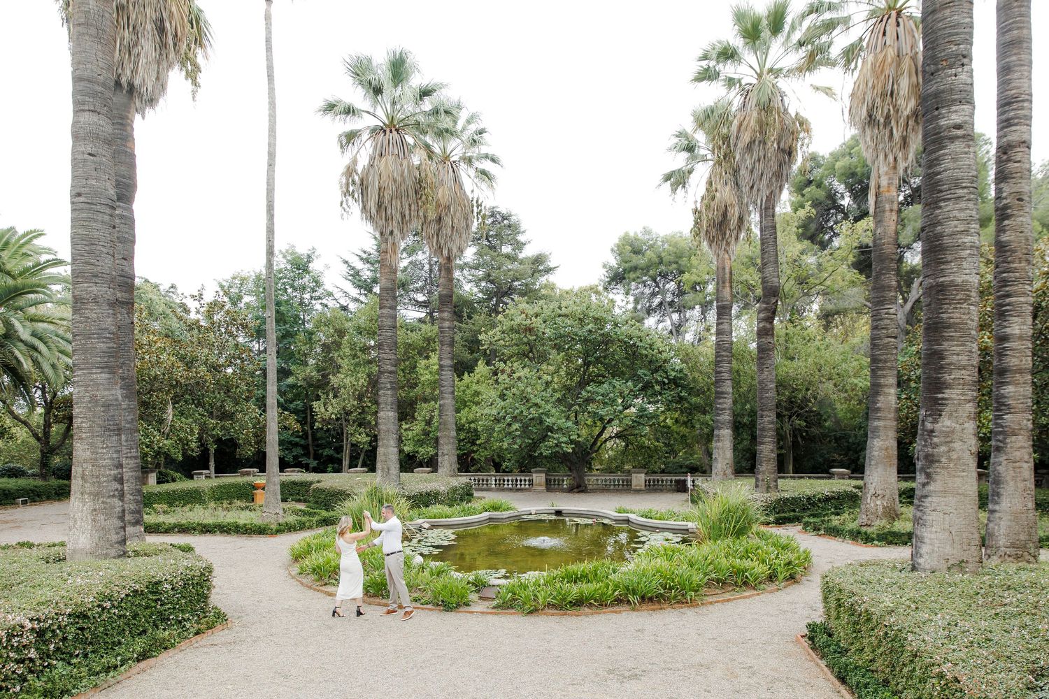 A couple dance among high trees and palms  during their engagement photo session in Barcelona