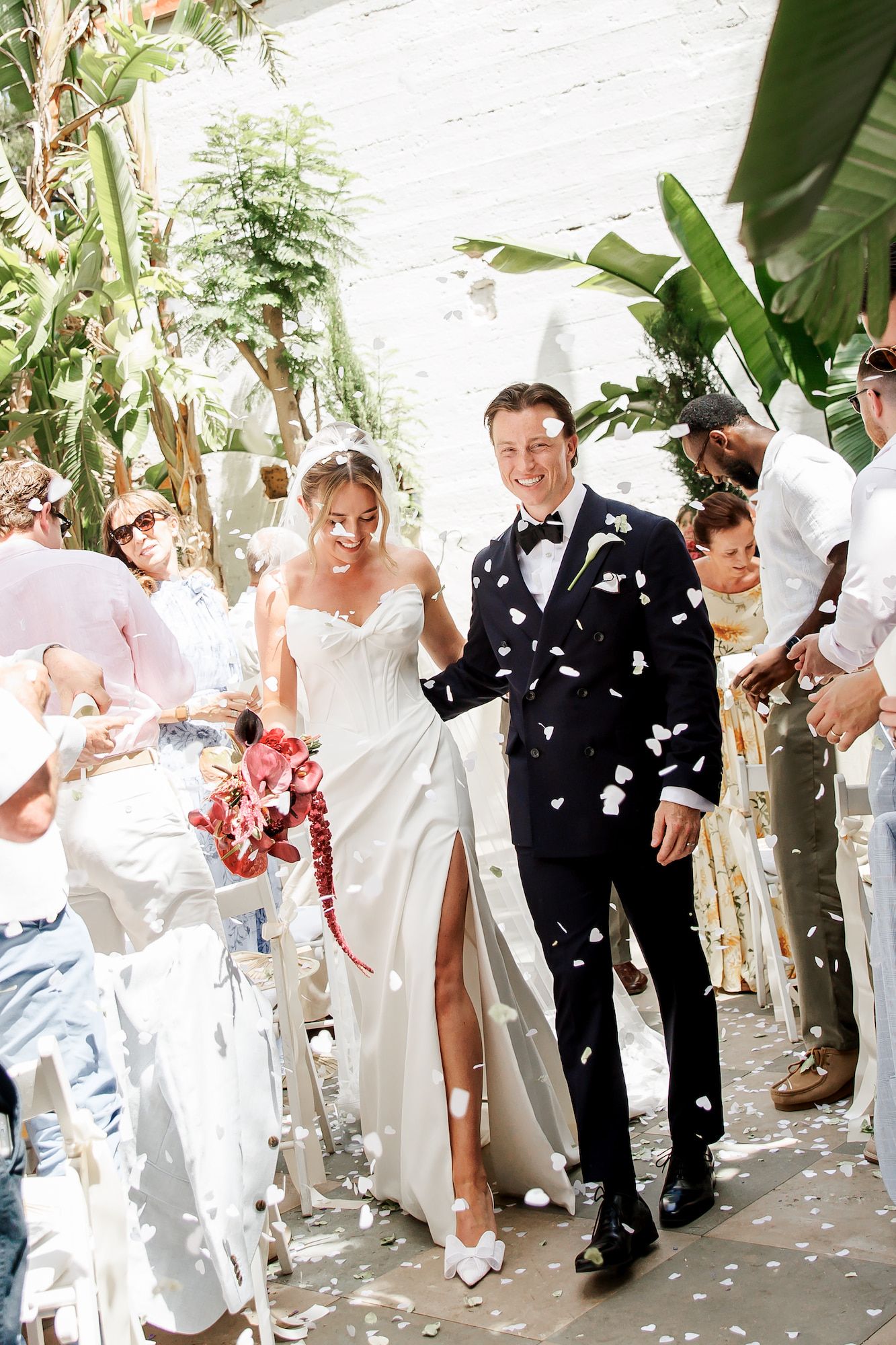 The bride and groom walk down the aisle as guests toss white confetti petals at an outdoor wedding ceremony near Barcelona
