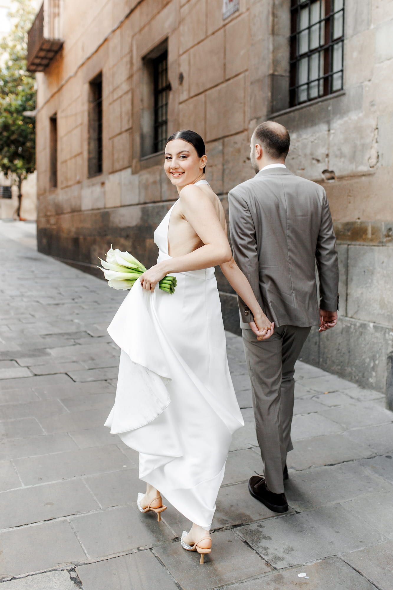 Bride in white dress playfully pulls groom in gray suit along a stone walkway in a sequence of candid photos.