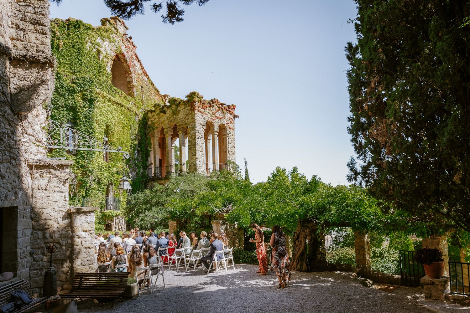 Outdoor wedding ceremony at La Baronia covered in ivy, with guests seated under lush trees | La Baronia | Wedding Photographer Barcelona