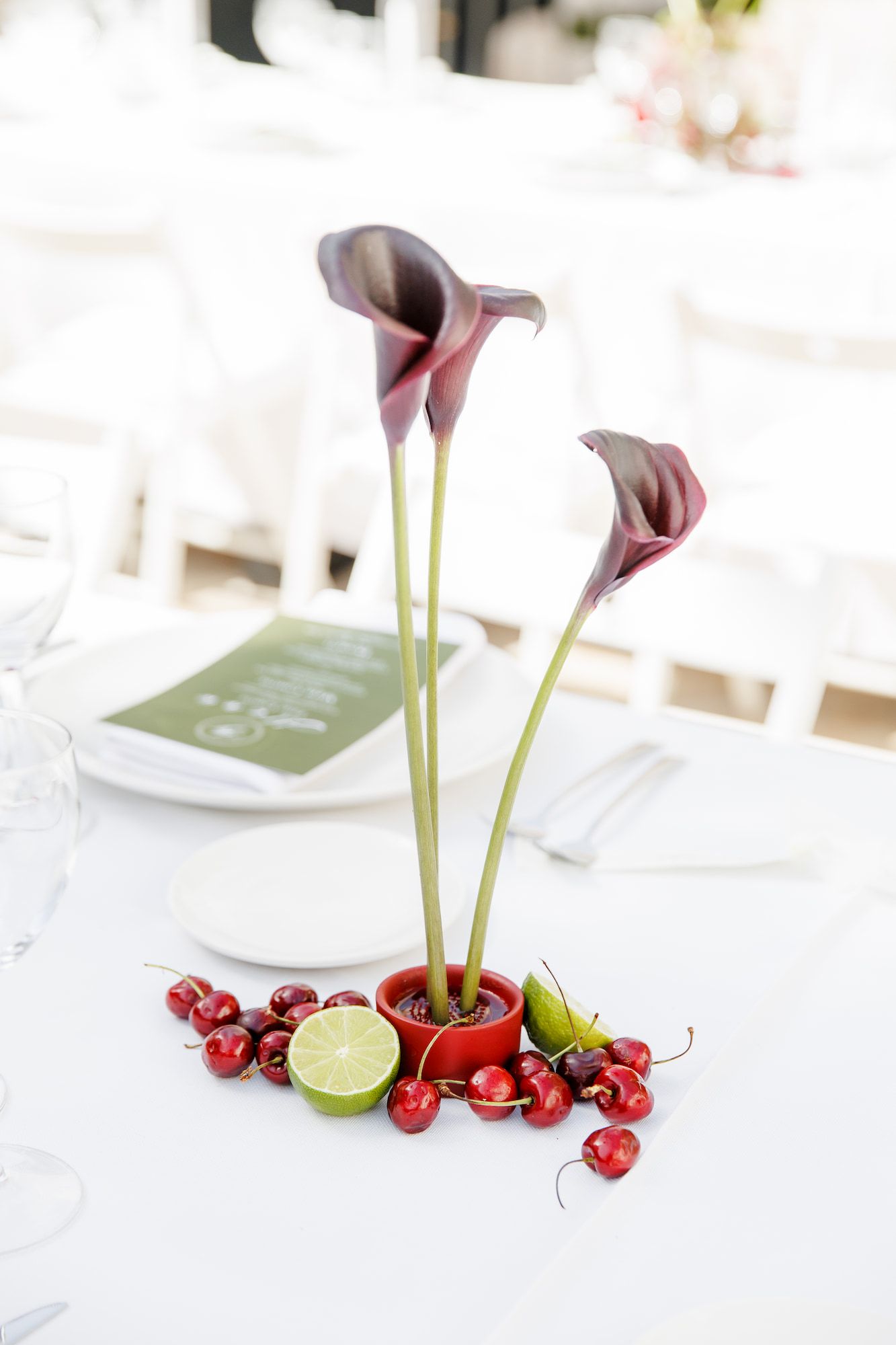 Elegant table centerpiece with dark calla lilies in a red pot.