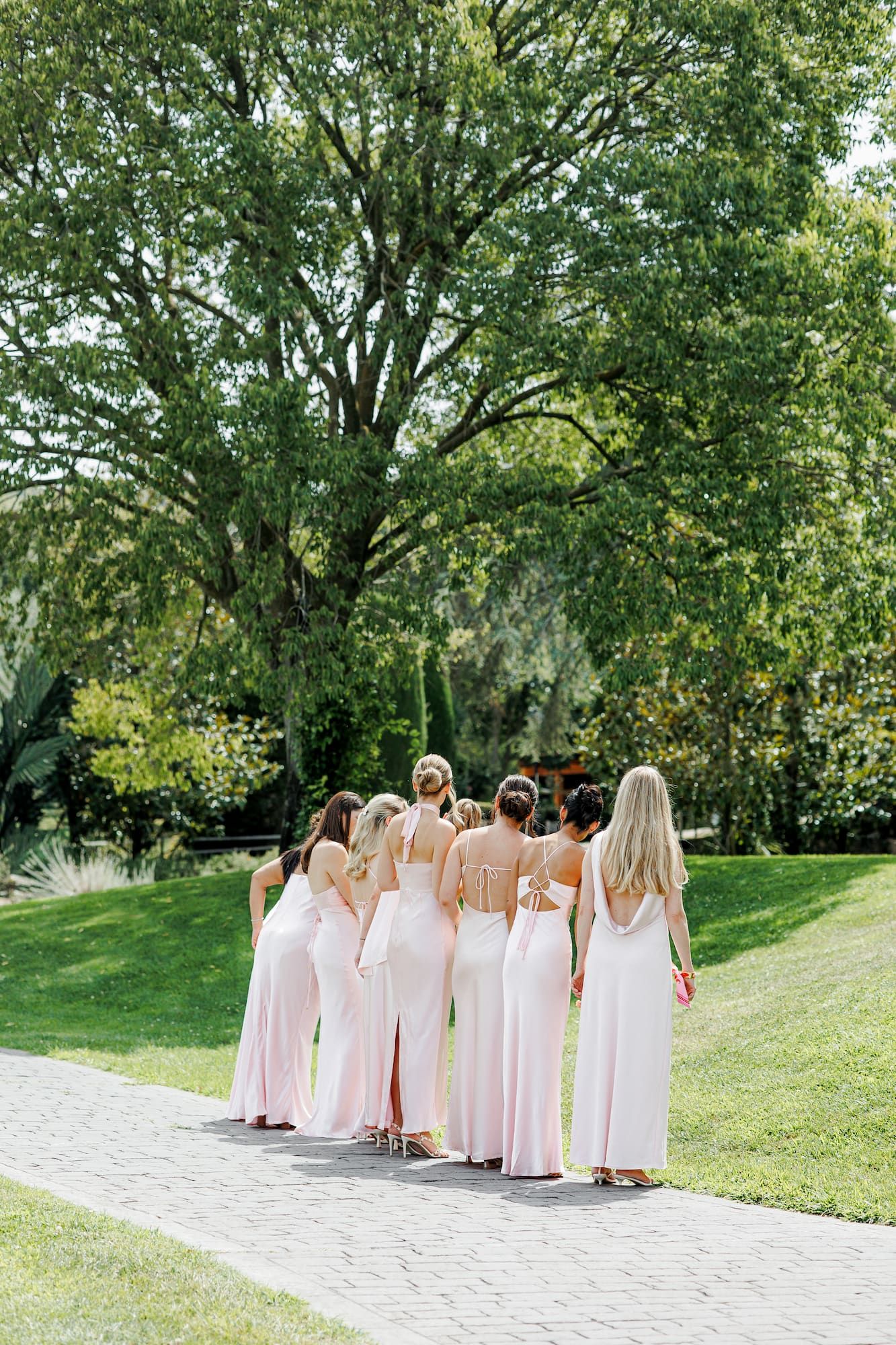 Bridesmaids in pink dresses walk along a garden at the wedding venue in Barcelona.