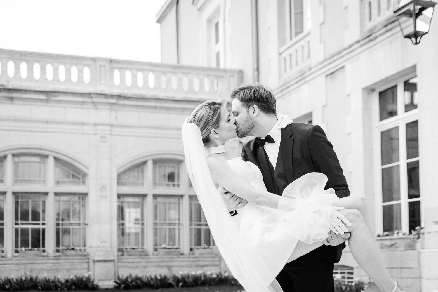 The groom is carrying the bride on hands and kisses her on the way to the wedding dinner