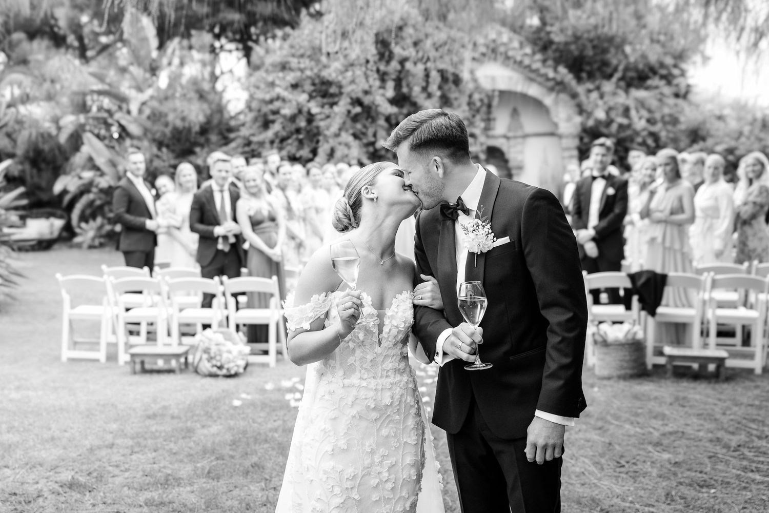 The groom gives a gentle kiss to the bride while they hold glasess with cava.