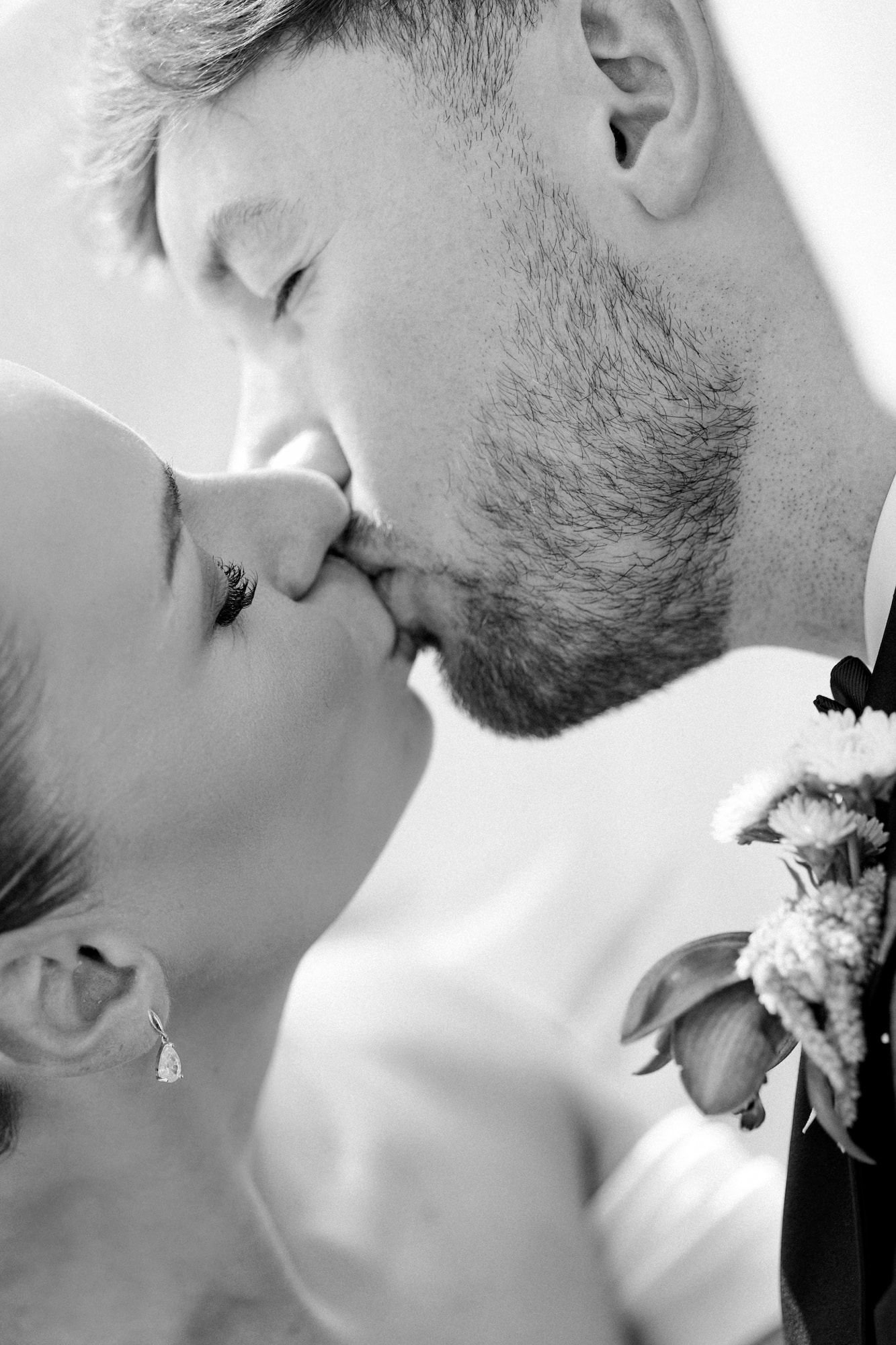 Black and white photo of a bride and groom sharing a romantic kiss, with the bride holding a bouquet of flowers.