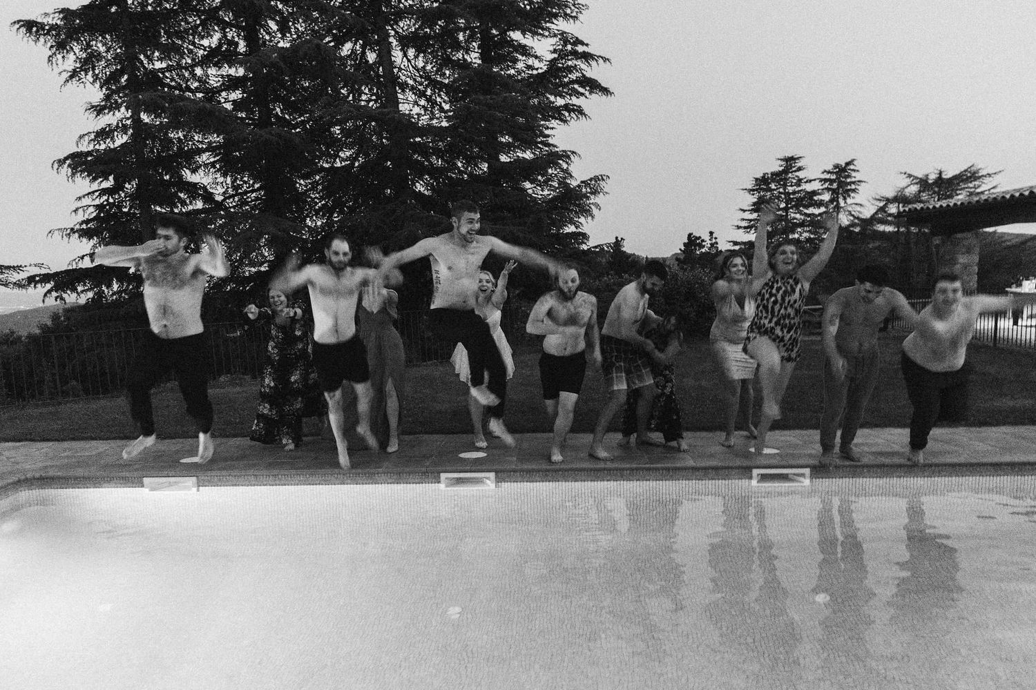 A black and white photo of a group jumping in a swimming pool.