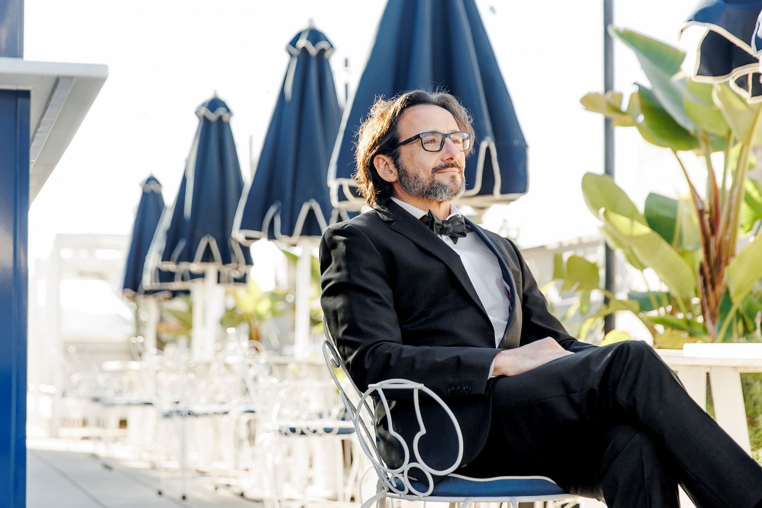 A groom wearing sunglasses and dark clothing relaxes in a white chair on the terrace of Barcelona