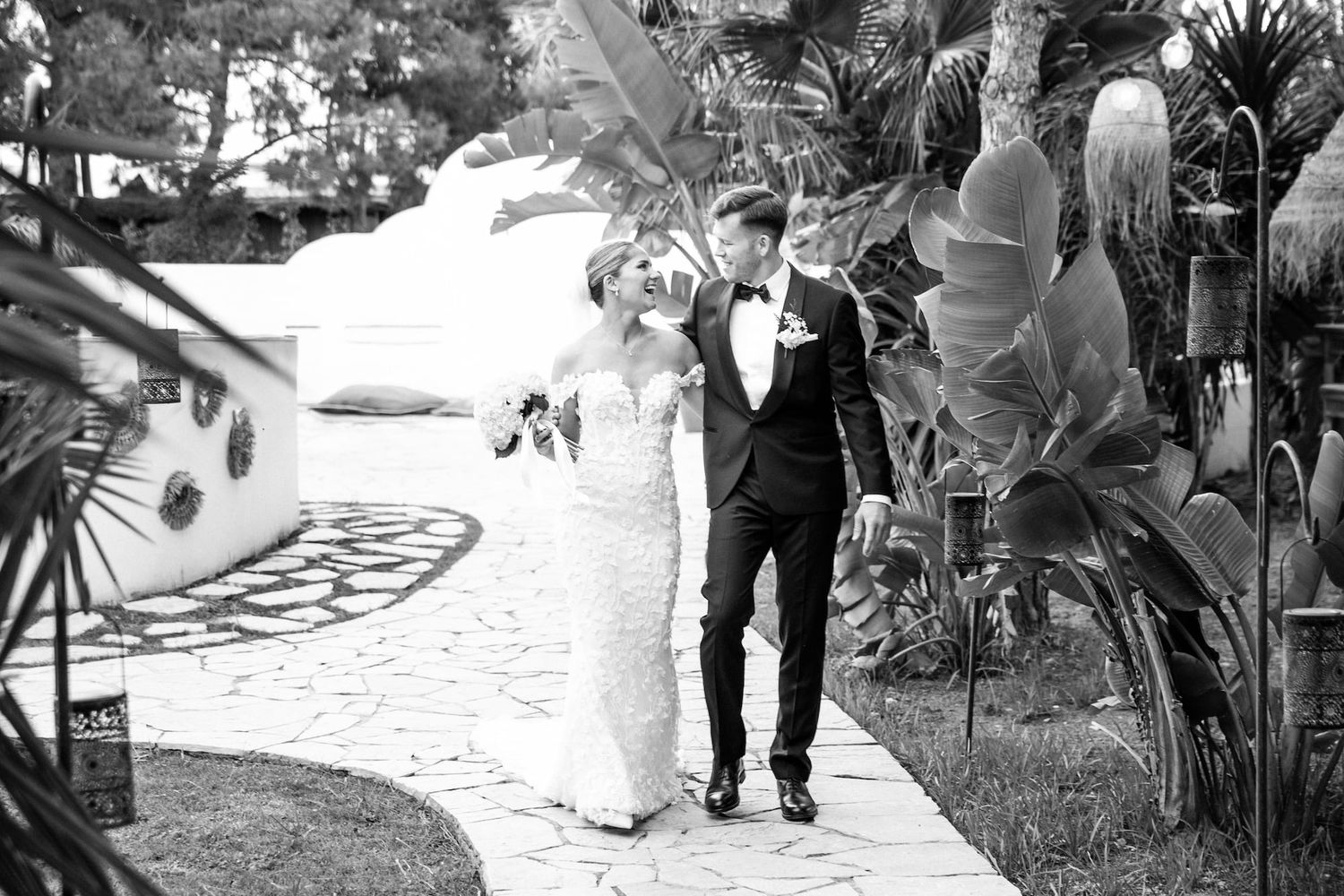 A black and white wedding photo of a couple is walking in the gardens of Gran Villa Rosa
