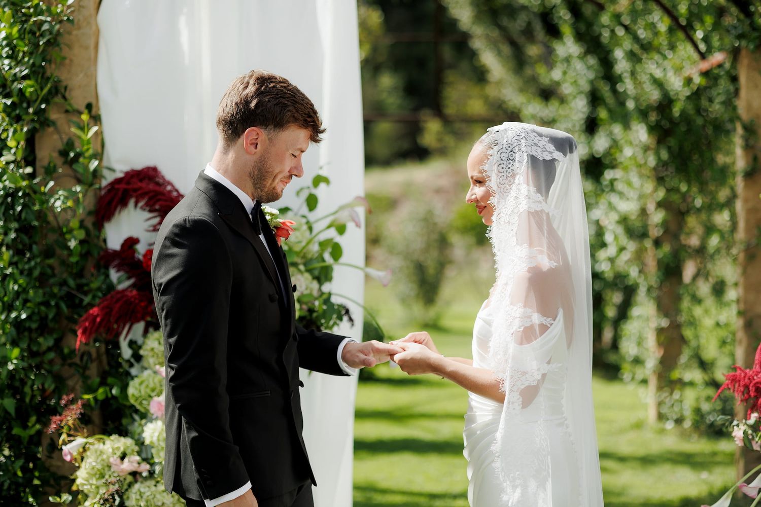 Bride and groom exchanging vows at an outdoor wedding ceremony with floral arch backdrop.