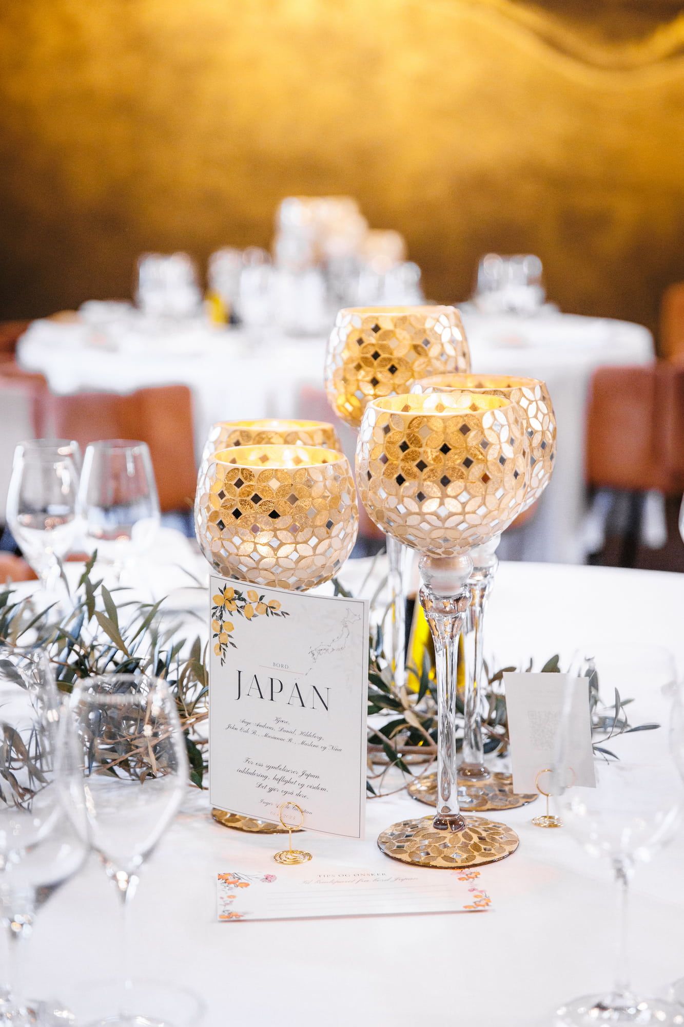 Elegant wedding table centerpiece with gold mosaic candle holders and a Japan-themed place card on white linen.