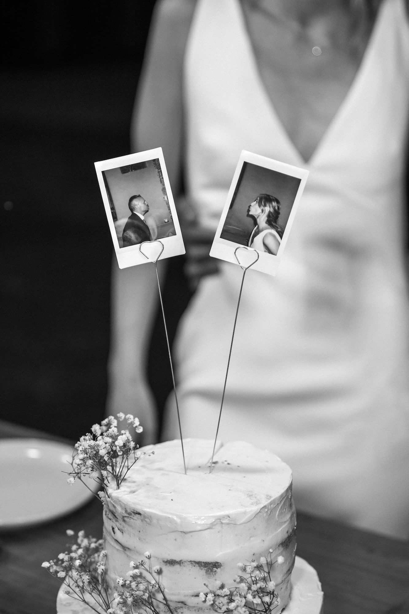 Black and white photo of a wedding cake topped with Polaroid photos of the bride and groom at Castel de Sant Marcal